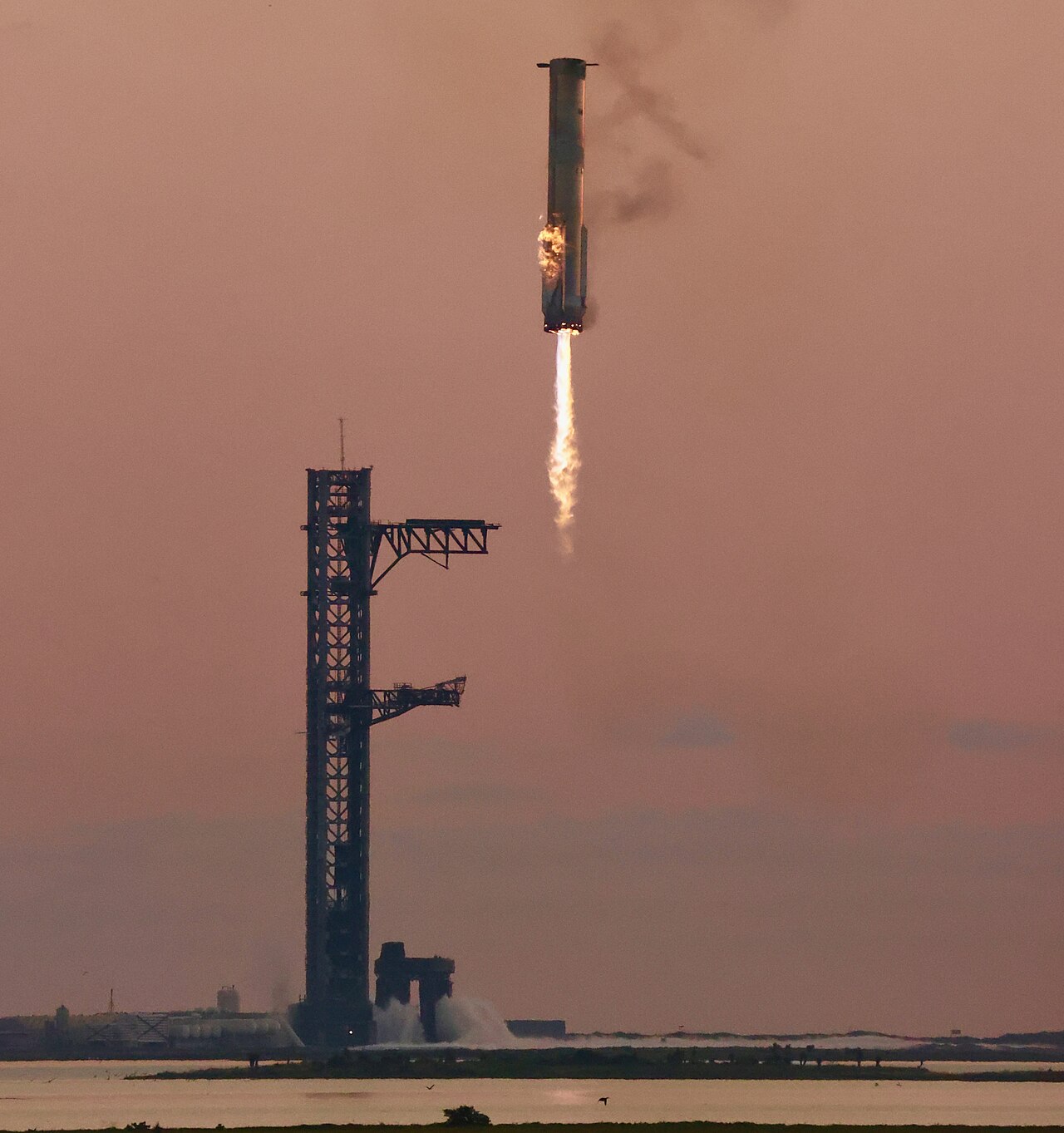 スペースXのスターシップブースターが高い打ち上げ塔から火炎を噴き出しながら垂直に上昇する様子
