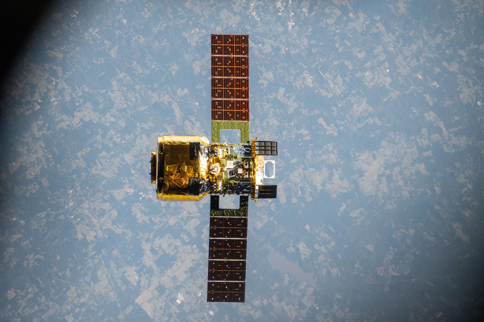 地球上空から撮影した人工衛星で、太陽光パネルを広げた状態で地球を背景に浮遊している様子。